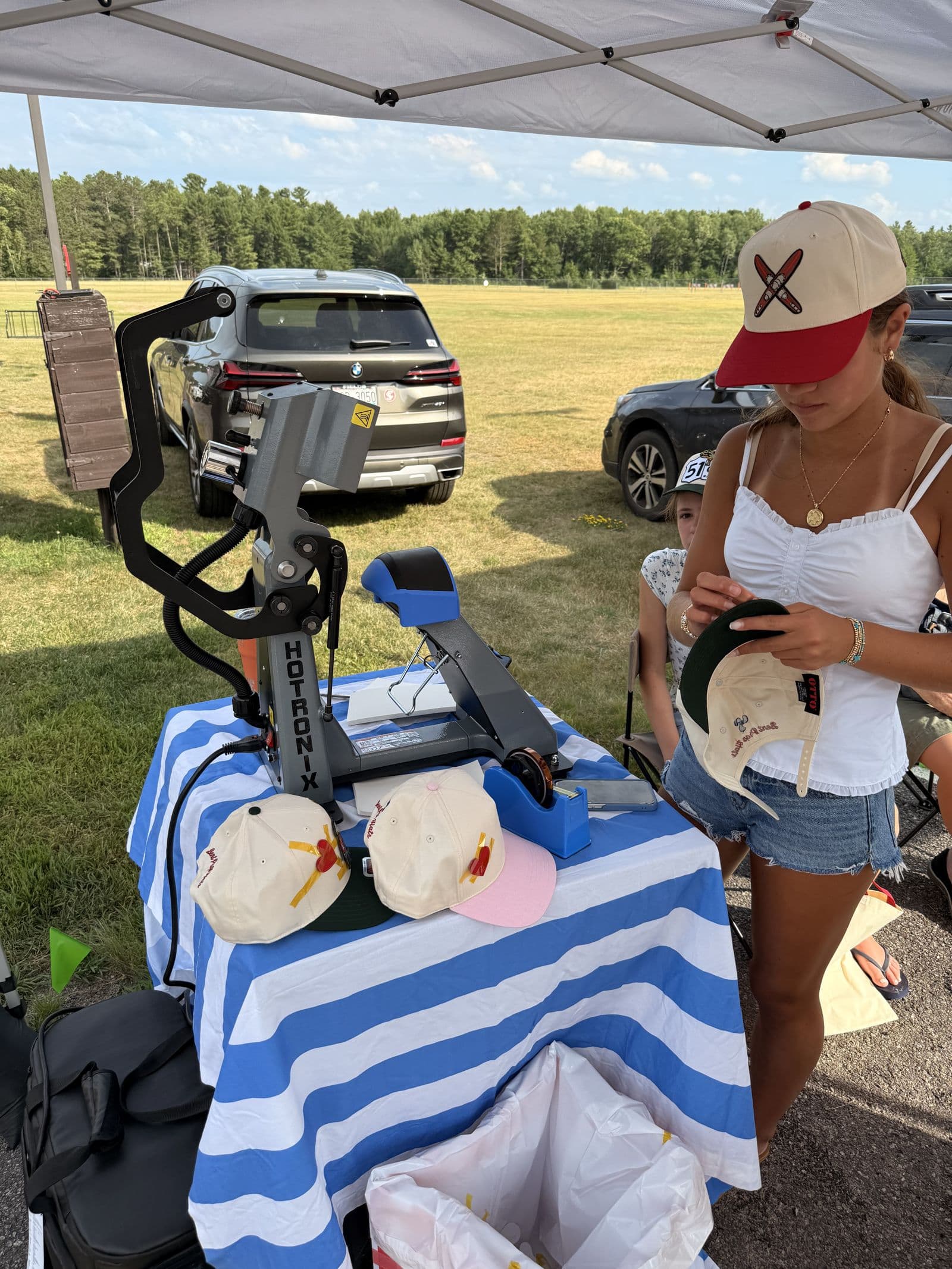 Pressing a hat at the Bent Prop tent, hats stacked on the striped table